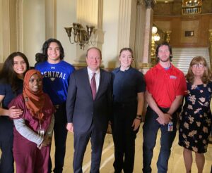 Photo of young people standing with Governor Polis of Colorado in the Colorado State Capitol building