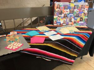 A display table with a colorful striped tablecloth, a display board of staff portraits, and sweet treats.