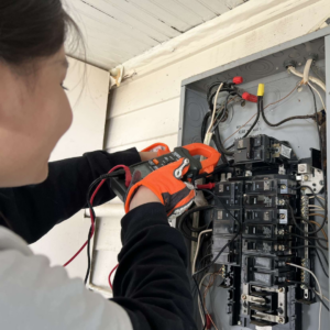 Image of Paola Cosio working on wiring a panel board, also known as an electrical breaker box.
