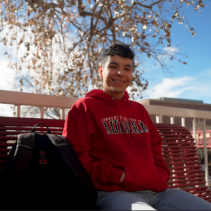 Image of Omar Temprana smiling and sitting on a bench at Community College of Aurora's campus.